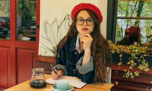 pexels-photo-4442128-4442128 A woman in a red beret writes in a notebook at a cozy café, exuding a vintage vibe.